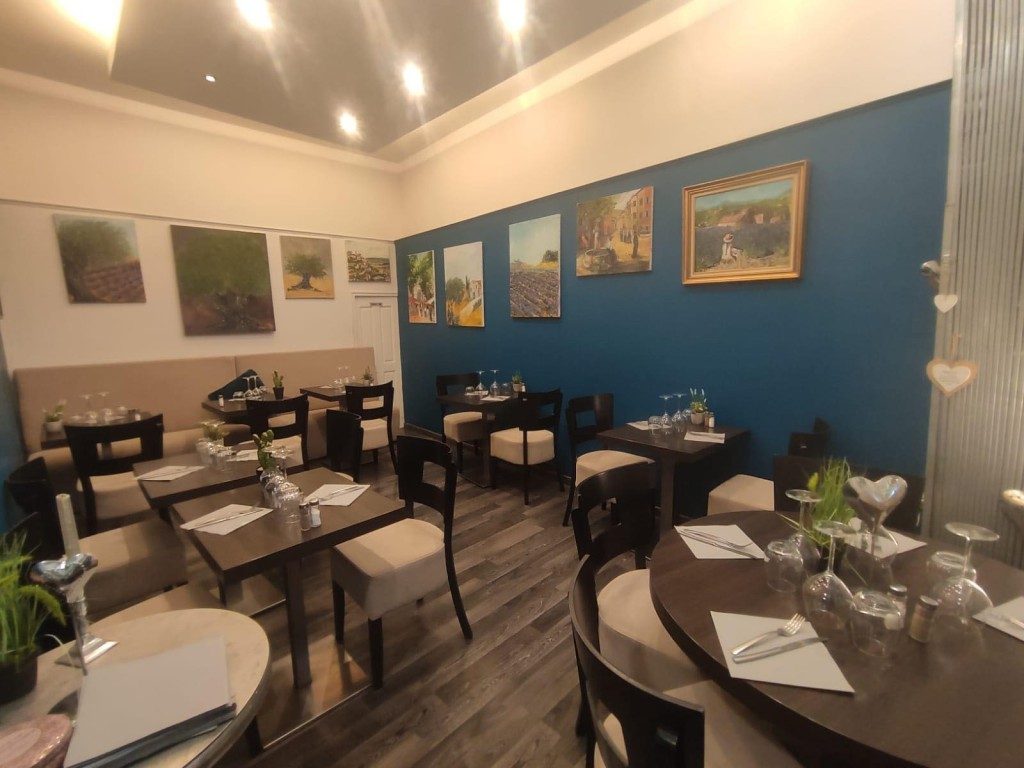 La salle du restaurant, tables dressées sous des tableaux aux murs bleus