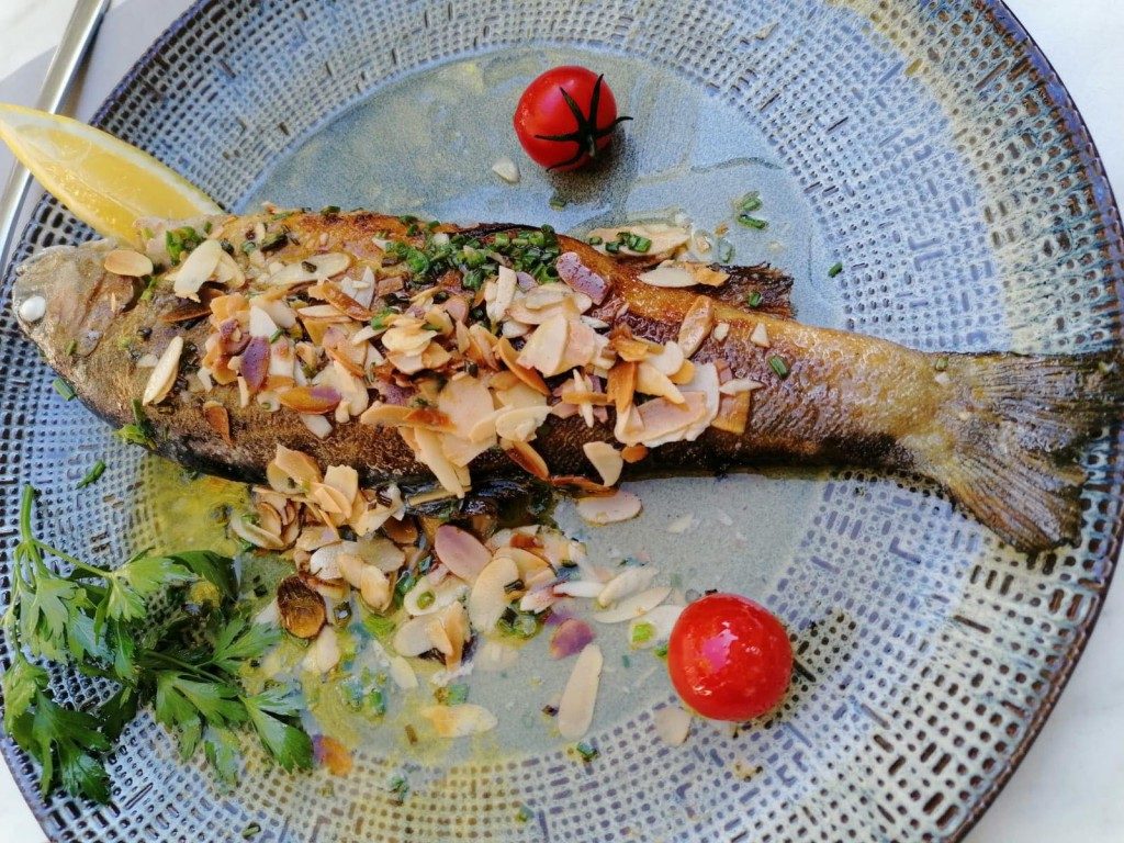 Une truite entière aux amandes effilées, avec des tomates cerises et du citron, sur une assiette bleue